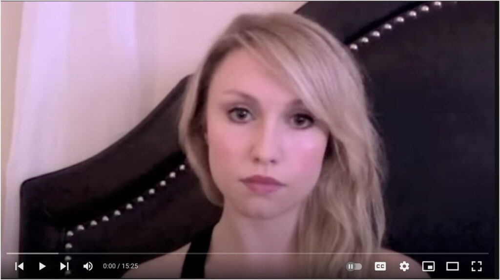 Screenshot of Blonde in the Belly of the Beast video. A blonde woman with a side part stares into the low resolution laptop camera.